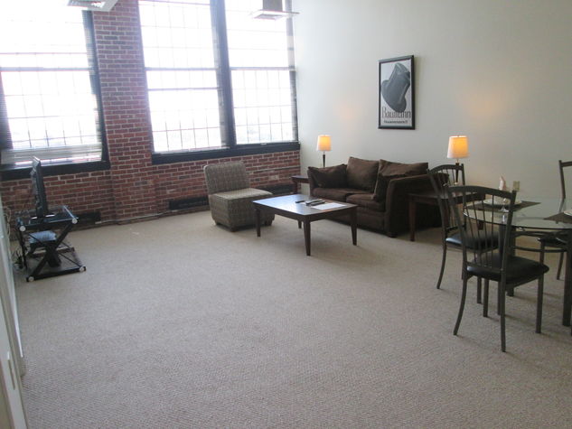 Spacious living room with over-sized windows providing lovely natural light, high ceiling and exposed bricks