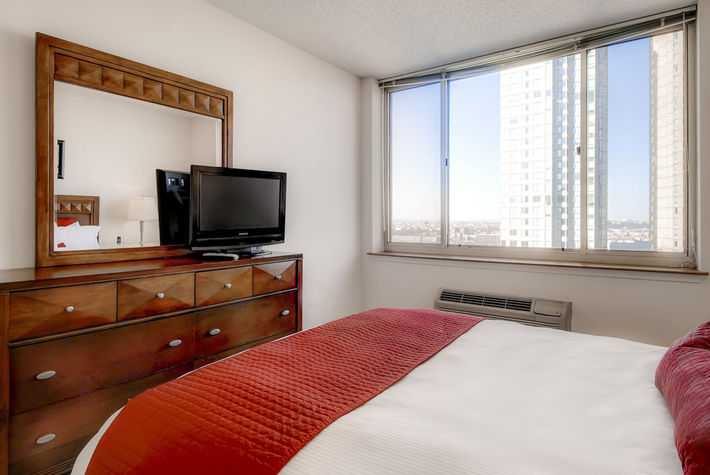 The bedroom features a dresser, a flat screen TV and a deluxe queen size bed with our indulgent custom linens, fluffy duvet, and plush pillows