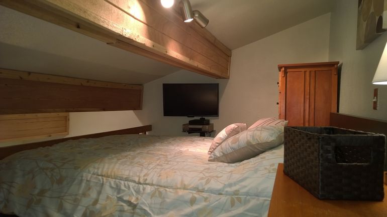 Comfortable queen-size bed in upper loft with flat-screen wall television and DVD player.