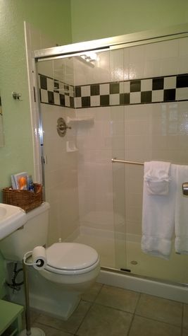 Renovated walk-in shower with flexible showerhead, pedestal sink, and high ceiling.